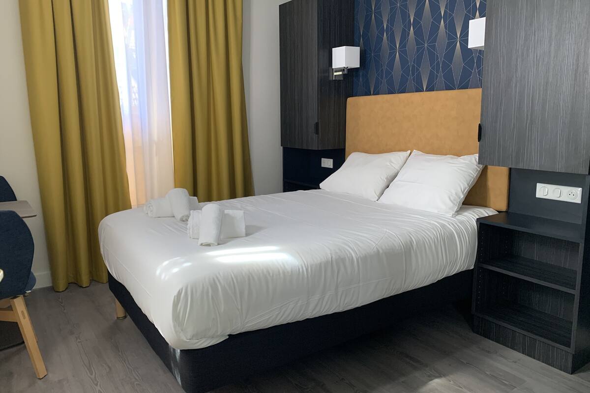 A neatly made bed with white linens, a dark headboard, and a bedside table with a lamp.