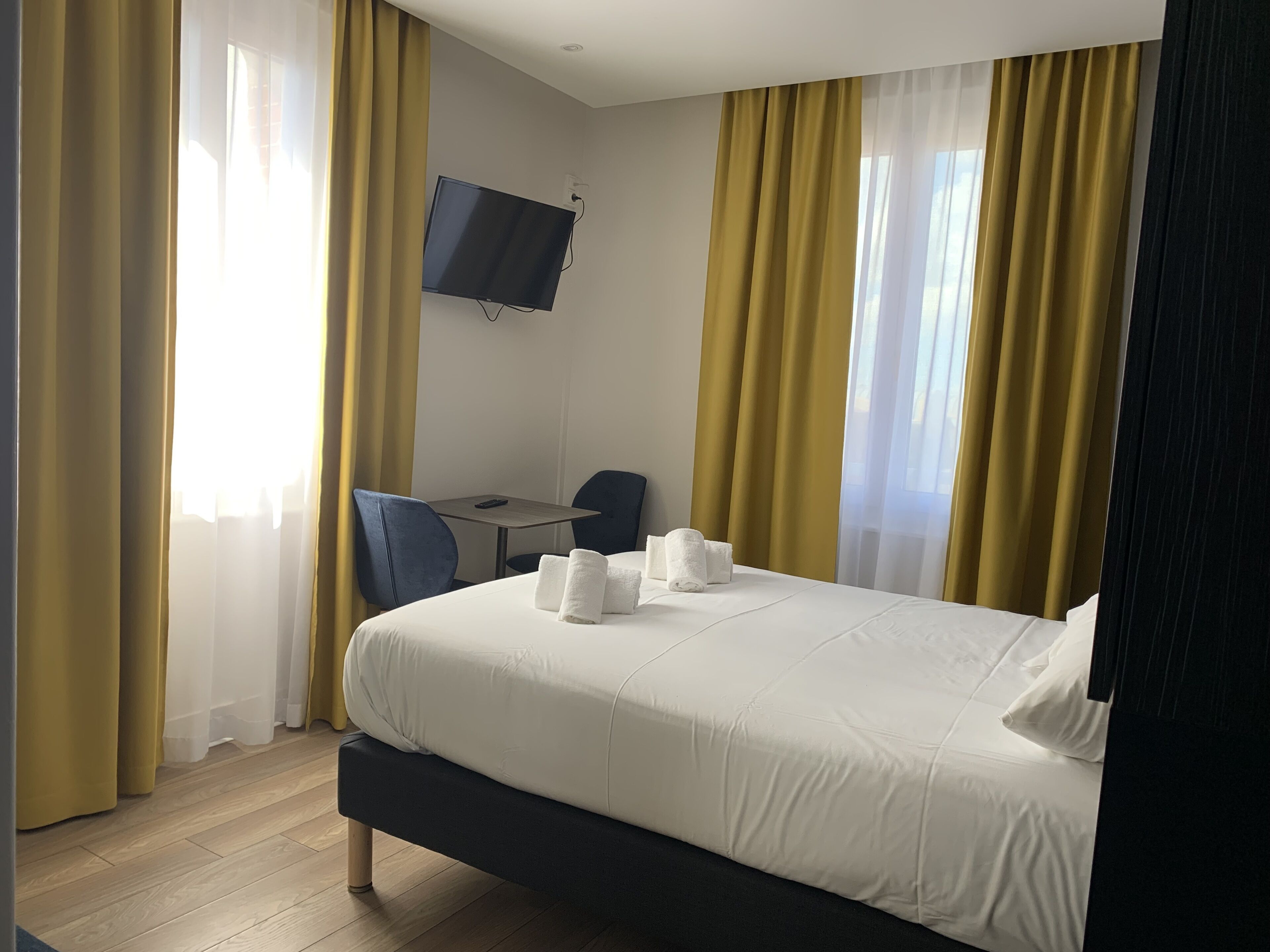 A hotel room with a bed, a desk, a chair, and a TV mounted on the wall.