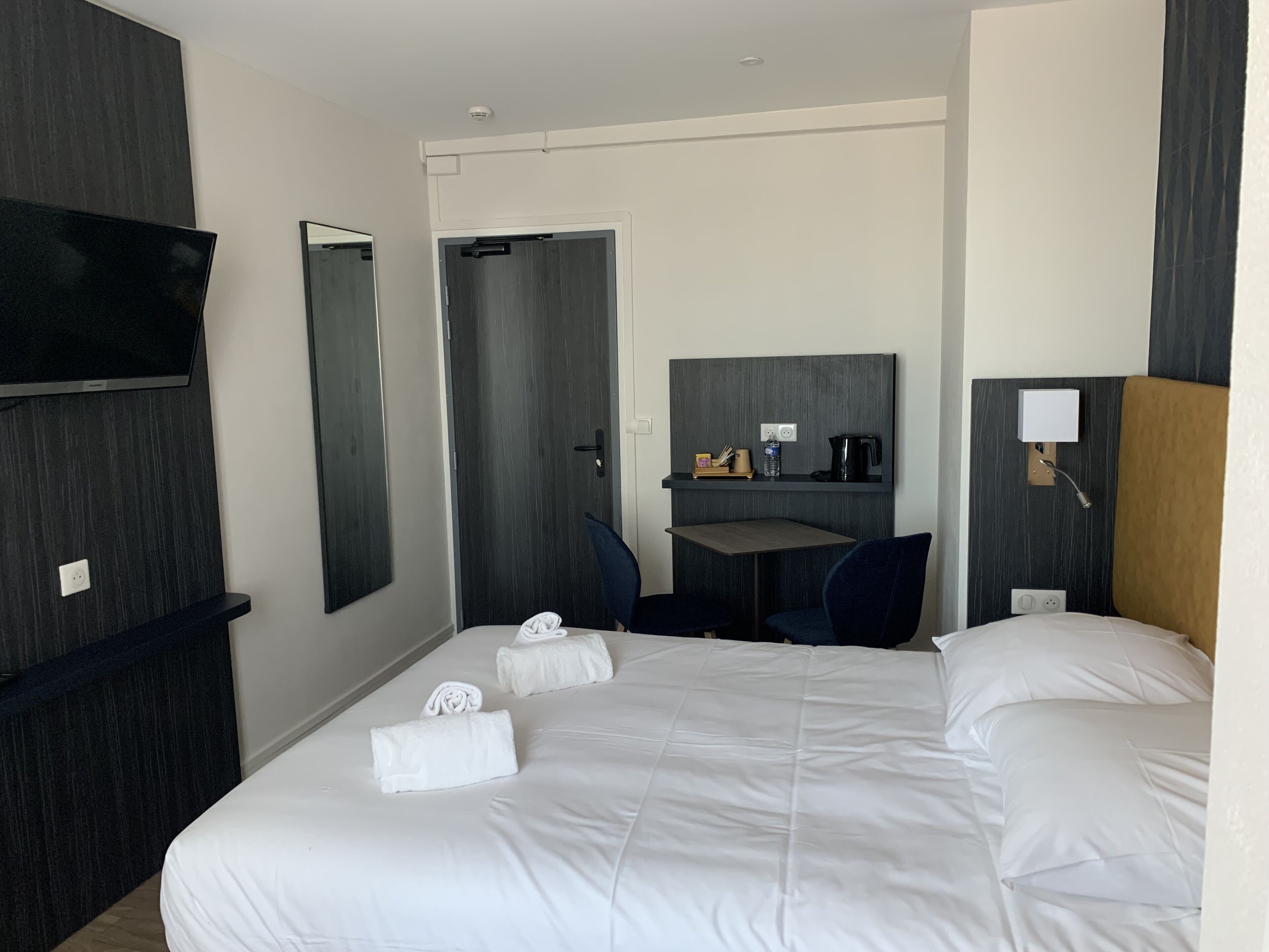 A hotel room with a bed, a desk, a chair, a flat-screen TV, and a mirror.