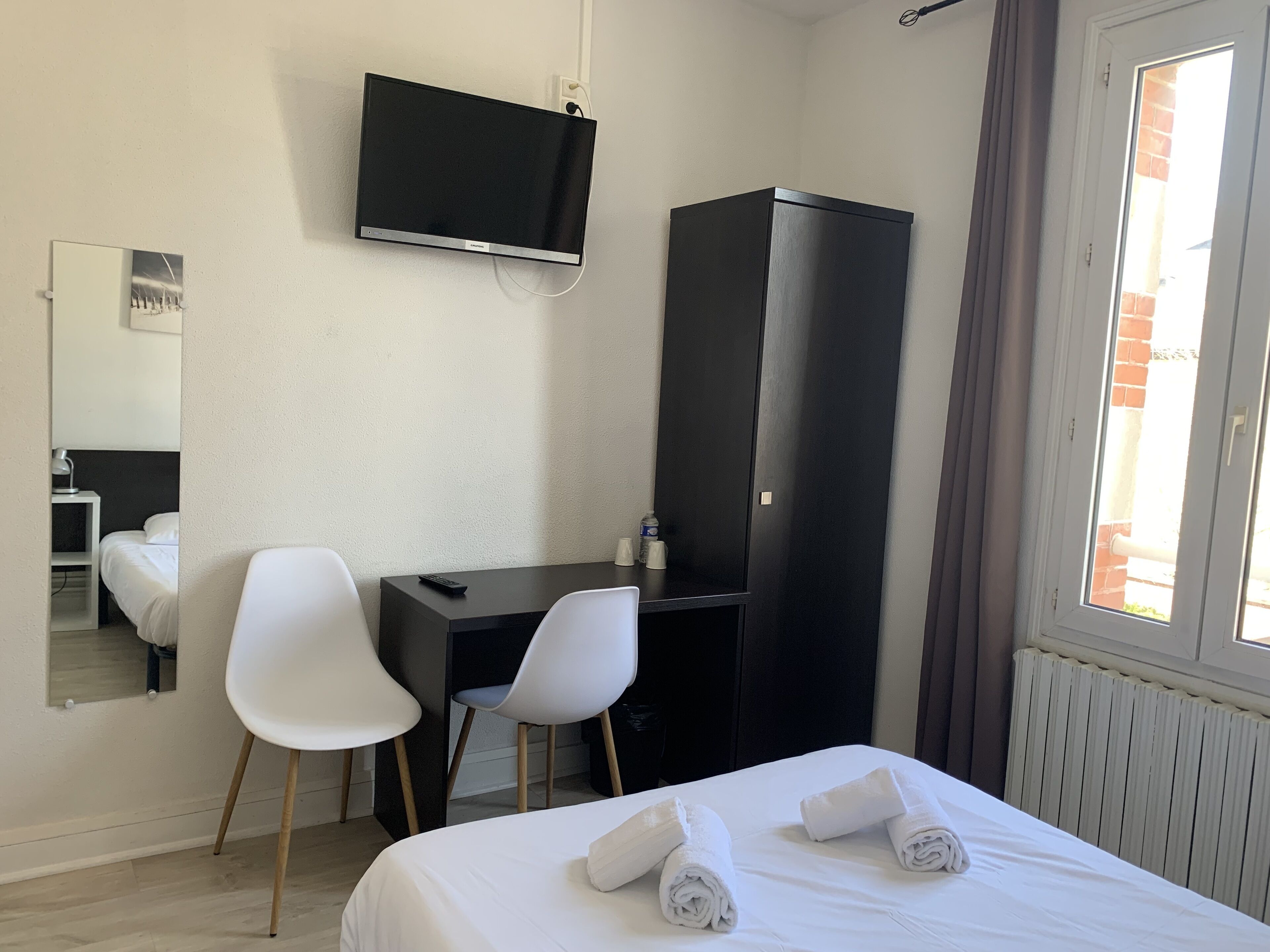 Una habitación de hotel con una cama, dos sillas blancas, un escritorio, un televisor y un armario.