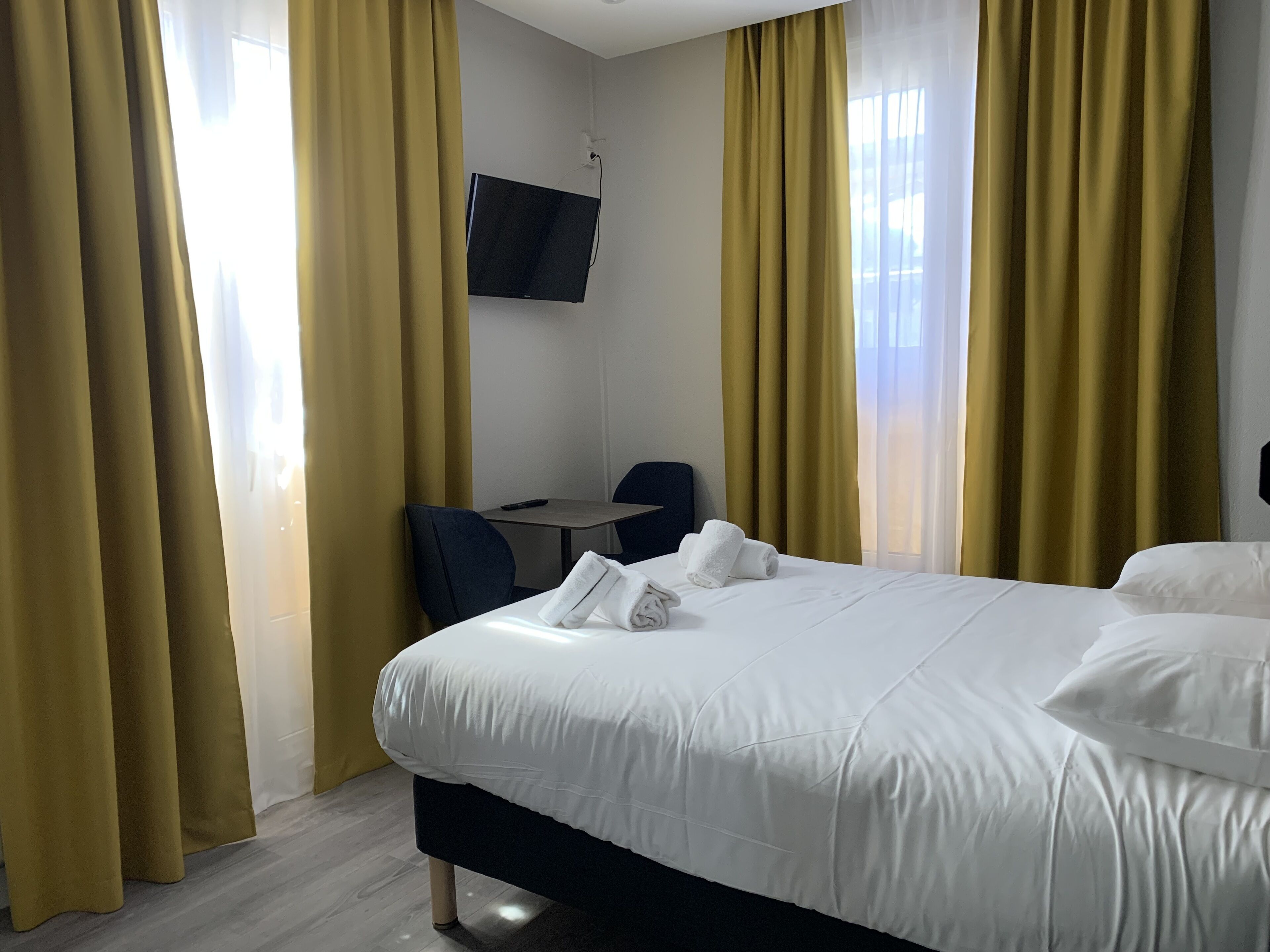 Une chambre d’hôtel avec un lit, un bureau, une chaise et un téléviseur fixé au mur.