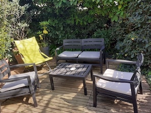 Un patio con un pavimento in legno, due poltrone grigie imbottite, una sedia gialla e un tavolino.