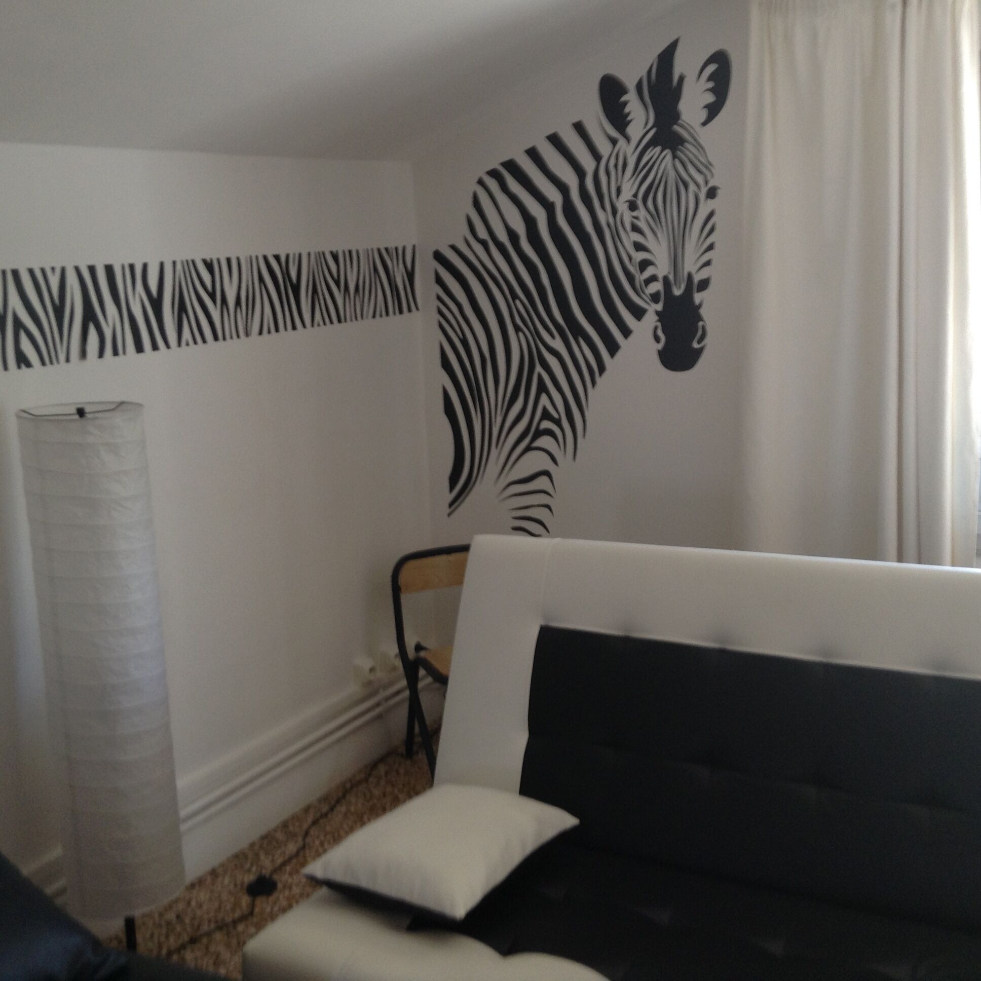 A room with a zebra wall decal, a sofa, a chair, and a floor lamp.