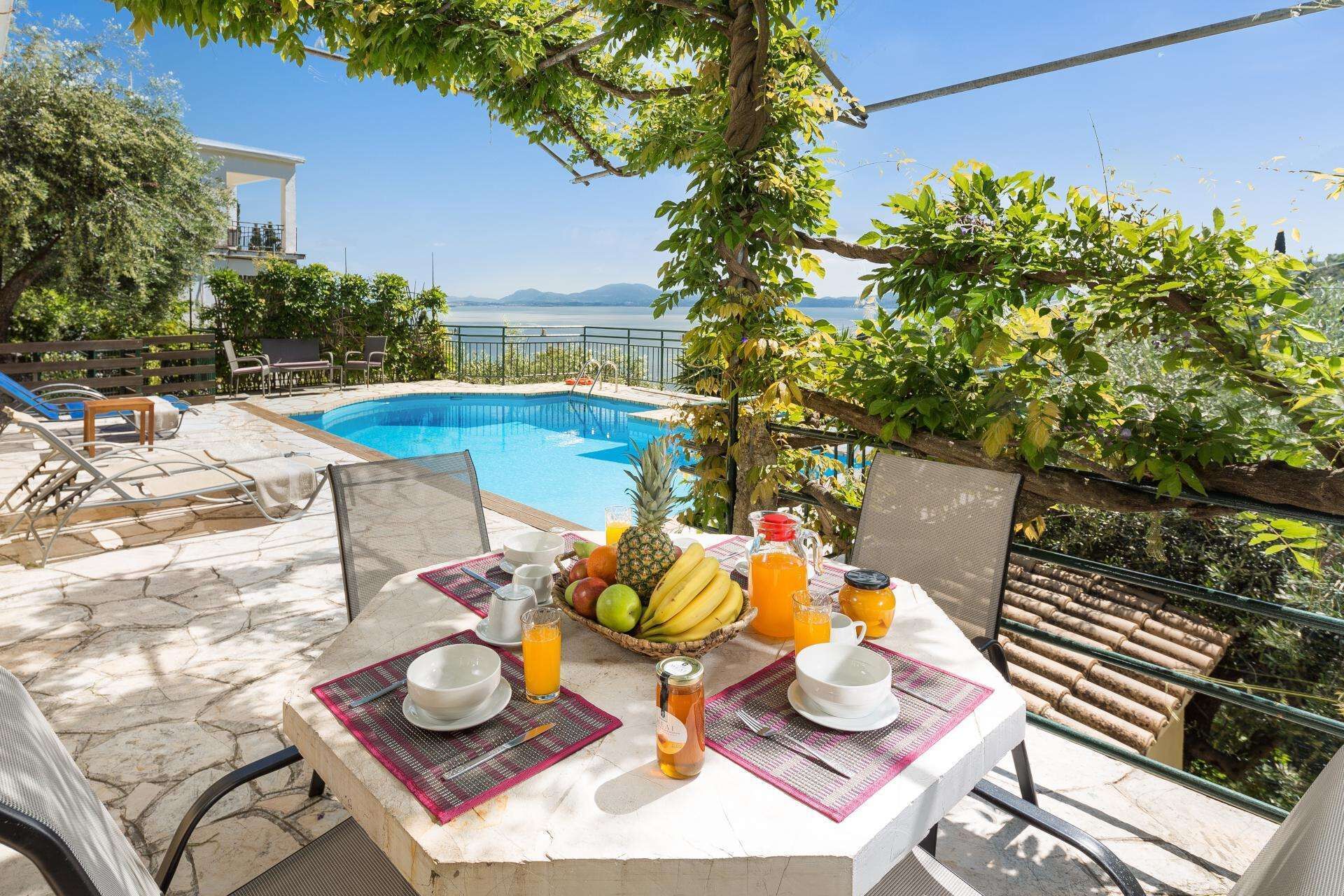 A poolside breakfast setup with a table, chairs, and a view of the pool and mountains.