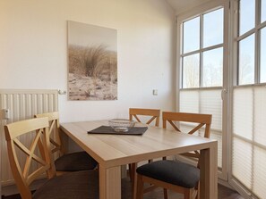 Ein Essbereich mit Holztisch und Stühlen, einem Bild an der Wand und einem Fenster mit Jalousien.