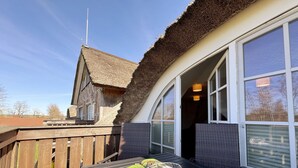 Un ponte di legno con un tavolo, una sedia in metallo e un edificio con tetto di paglia sullo sfondo.