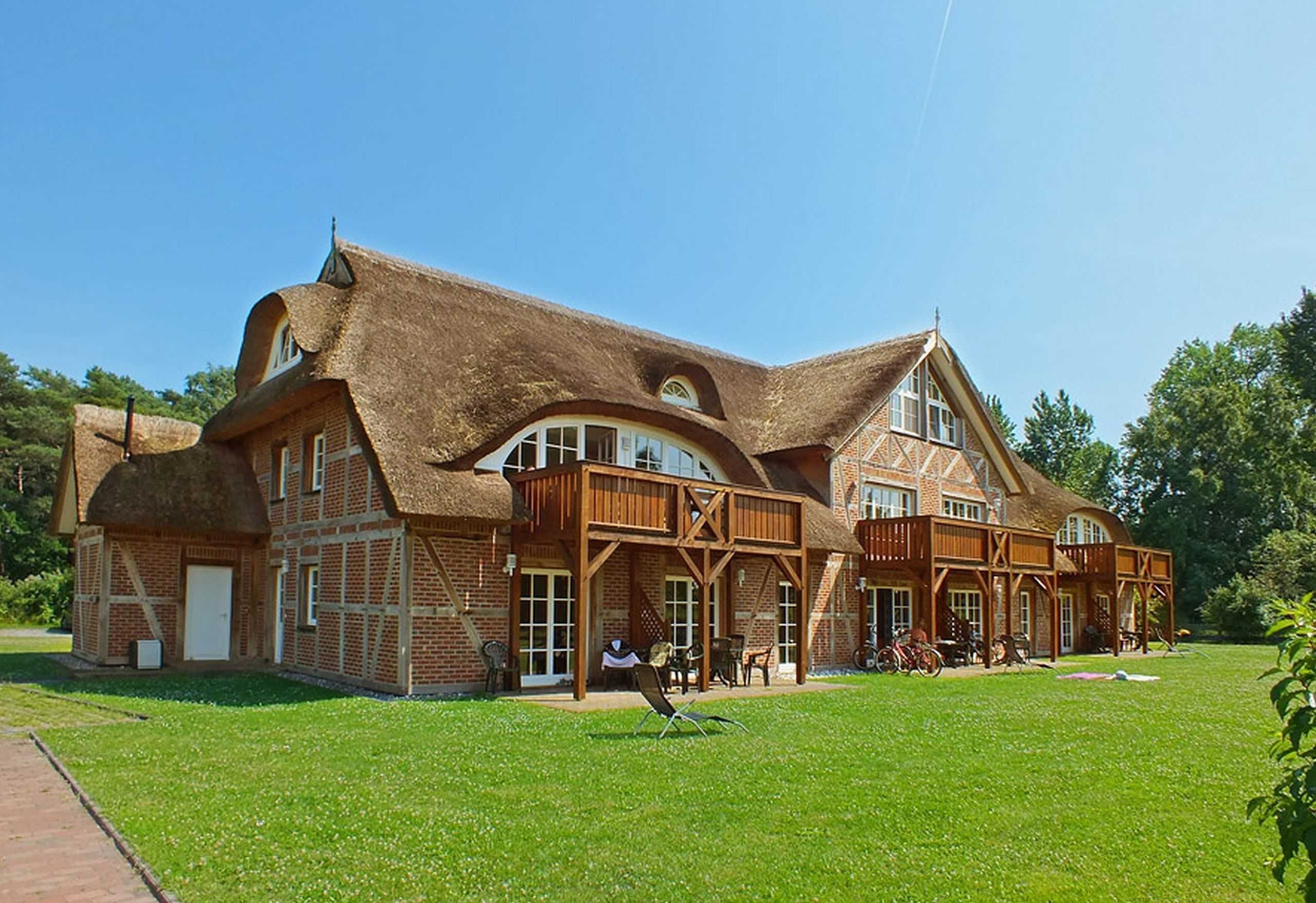 Een groot, landelijk gebouw met rieten dak en bakstenen muren, met een ruime patio en terrasmeubilair.