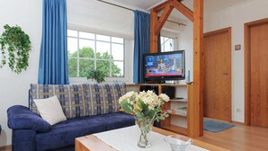 Una sala de estar con un sofá azul, una mesa de centro, un televisor sobre un mueble de madera y una ventana con cortinas azules.