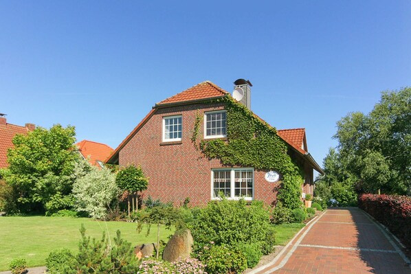 A brick house with a red-tiled roof, ivy-covered walls, and a visible chimney.