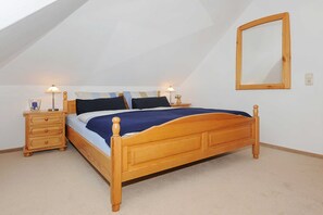 A bedroom with a wooden bed, two bedside tables, a nightstand, a mirror, and a sloped ceiling.