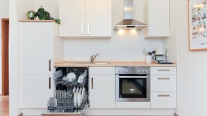 Una cocina moderna con armarios blancos, lavavajillas, horno y cafetera.