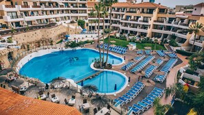 Ett semesterhotell med en stor pool i mitten, flera balkonger och ett välskött trädgårdsområde.