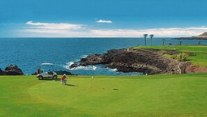 En golfbana vid kusten med fri utsikt över havet och en kuperad, stenig terräng.