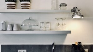 Cuina amb prestatges blancs que contenen vidrieres, una cafetera i plantes en testos.