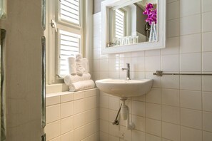 Une salle de bain avec un lavabo blanc, un miroir et une fenêtre avec des stores.