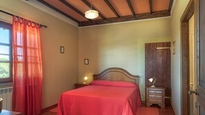 A bedroom with a bed, two bedside tables with lamps, a wooden door, and a window with curtains. - IL TASSO           . (Castiglione del Lago)