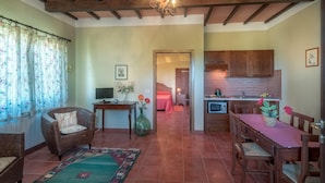 A spacious living area with a dining table, wicker sofa, and a kitchen in the background. - IL TASSO           . (Castiglione del Lago)