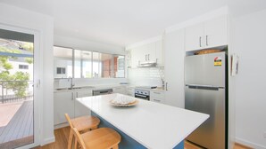A modern kitchen with white cabinetry, a stainless steel refrigerator, and a large island with a bowl of fruit. - Pippis on Pacific - fantastic two-level townhouse located opposite Yamba's beautiful Pippi Beach (Yamba)