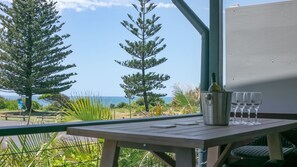 A balcony with a table, a bottle, and glasses, overlooking a coastal area with trees and the sea. - Pippis on Pacific - fantastic two-level townhouse located opposite Yamba's beautiful Pippi Beach (Yamba)