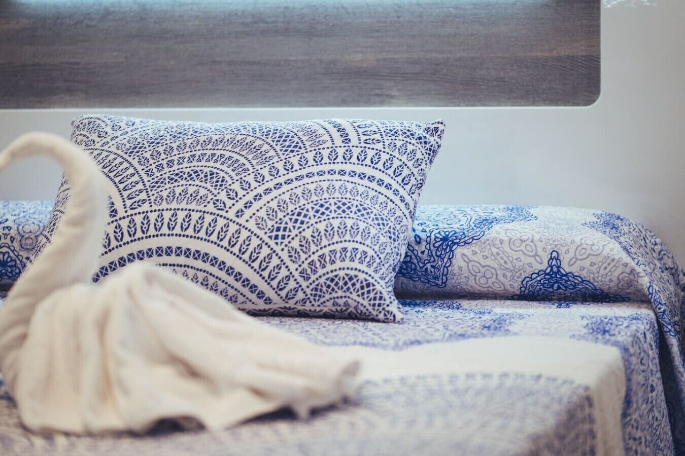 Una cama con una colcha azul y blanca estampada, un plaid blanco y un cabecero de madera.