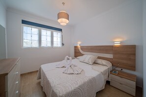 A bedroom with a bed, bedside tables, a wardrobe, a window, and a hanging light fixture.