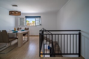 A dining area with a table set for four, a staircase with a black railing, and a window with a view of palm trees.