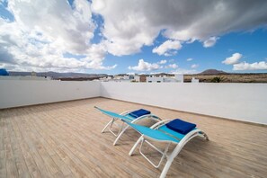 Eine Dachterrasse mit Holzboden und drei Liegestühlen.