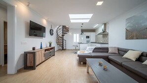 Un salon moderne comprenant un canapé, une table basse, un téléviseur, un meuble en bois, un escalier en colimaçon et un coin cuisine.