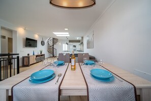 Ein moderner Essbereich mit einem langen Tisch, gedeckt für zwei Personen, einer Wendeltreppe und einer Küche im Hintergrund.
