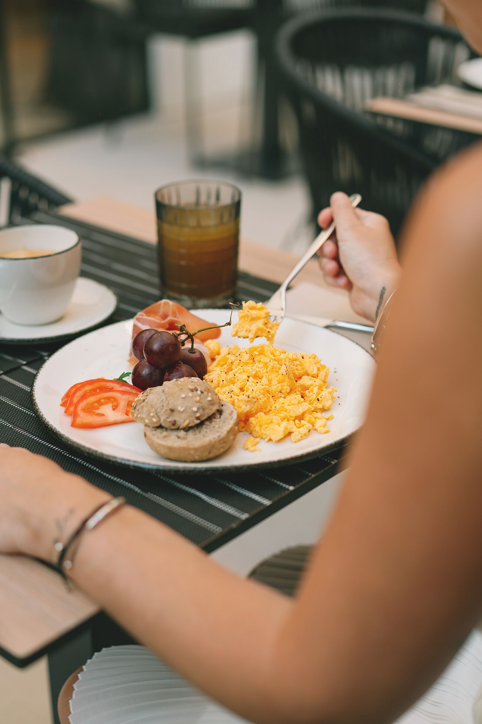 A breakfast plate with scrambled eggs, tomatoes, a slice of bread, and a glass of juice.