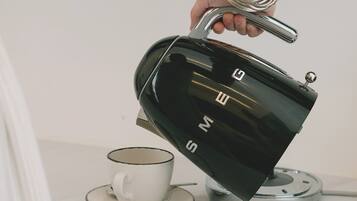 Une main tenant une bouilloire électrique noire dont on peut voir la marque, posée sur une surface blanche, à côté d’une tasse et d’une soucoupe blanches.