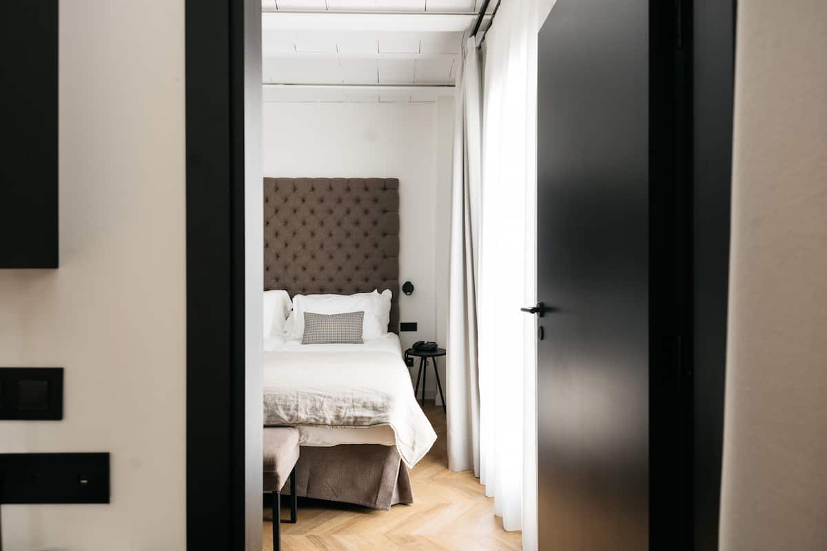 A bedroom with a bed, bedside table, and a door leading to another room.