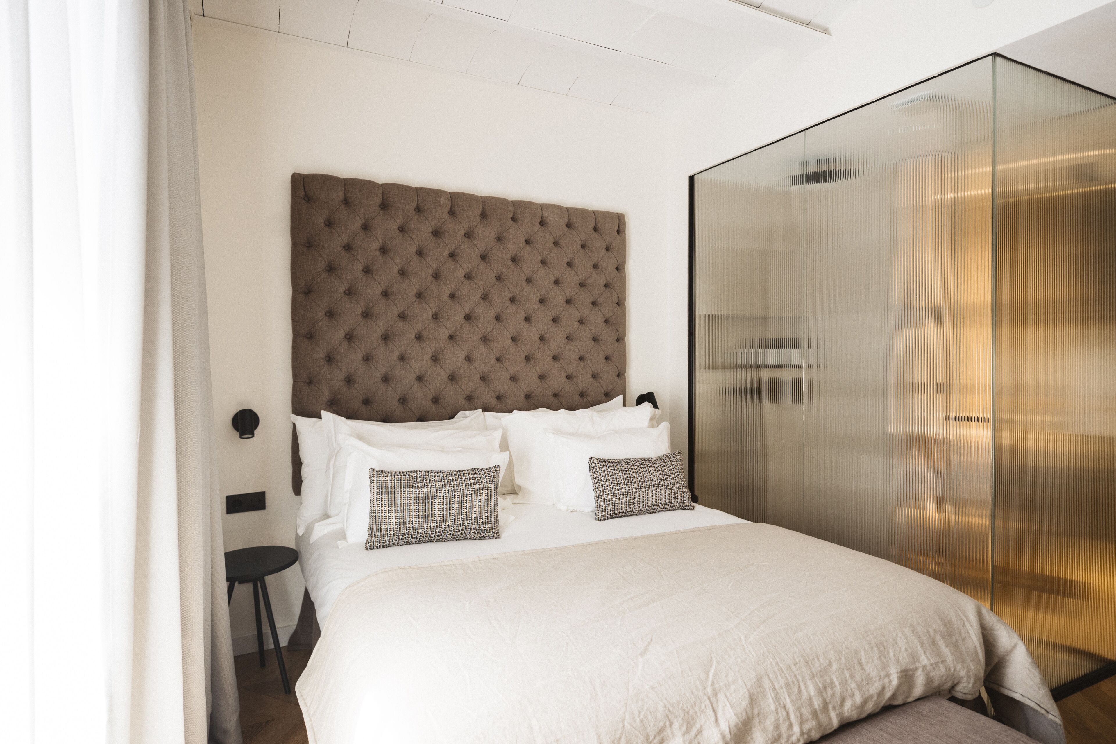 A modern hotel room with a large bed, a glass partition wall, and a small table.
