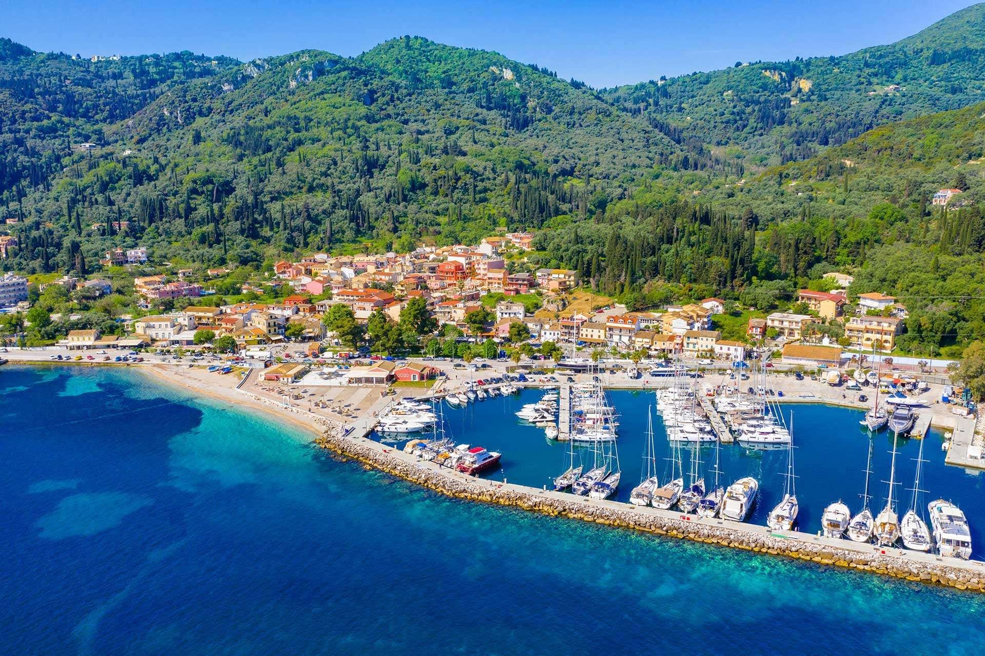 A coastal town with a marina, buildings, and a mountainous backdrop.