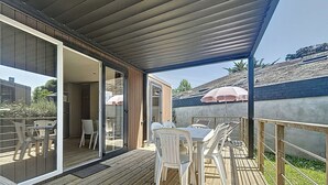 An outdoor deck with a wooden floor, white plastic chairs, and a table. - Luxury Mobile Home for 4, 200m from Beach, Pool, Fitness, Market Nearby (Jullouville)