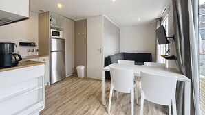 A modern kitchen with a microwave, refrigerator, and wooden countertop. There is a dining area with a white table and chairs. - Luxury Mobile Home for 4, 200m from Beach, Pool, Fitness, Market Nearby (Jullouville)