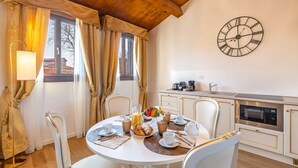 A dining area with a round table set for breakfast, a clock on the wall, and a kitchen in the background. - Laguna D 'oro Luxury Apartments - Exclusive Sky Suite (Venezia)