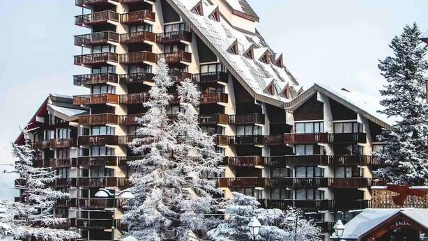 Un hôtel à plusieurs étages, doté de balcons, avec une piste de ski en arrière-plan.