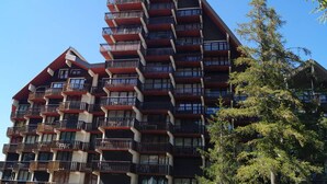 Un hôtel à plusieurs étages, doté de balcons à chaque niveau et entouré d’arbres.