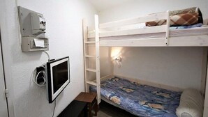 Une chambre avec un lit superposé, un bureau, un radiateur fixé au mur et une prise de courant.