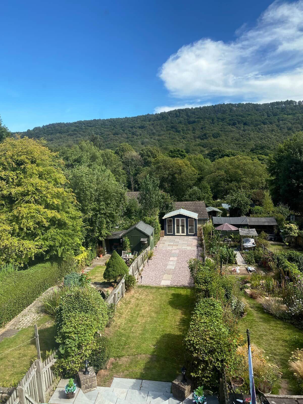 A residential property with a large garden, a patio area, and a view of a forested hill.