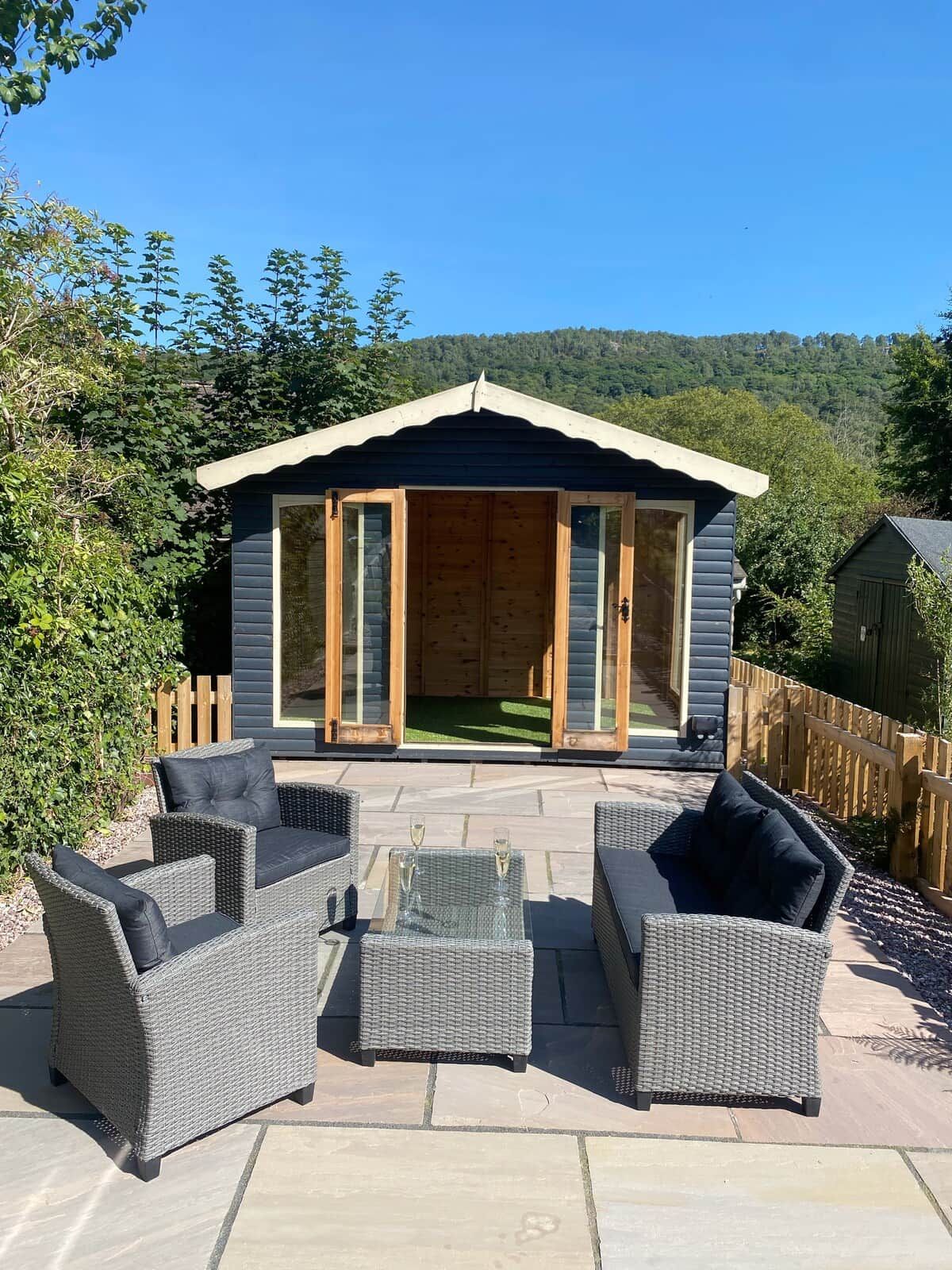 Eine Holzlaube mit Veranda, möbliert mit Korbmöbeln und einem Glastisch.