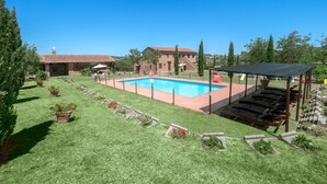 A backyard with a swimming pool, a covered seating area, and a brick building in the background. - IL RICCIO          . (Castiglione del Lago)