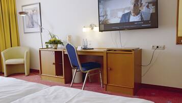 Habitación de hotel con cama, escritorio, silla, televisión y una pequeña mesa con un florero.