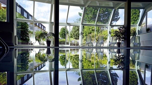 A conservatory with a glass floor, chairs, and potted plants. - AVALON Hotelpark Königshof (Königslutter am Elm)