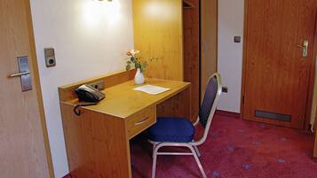 Un escritorio de madera con un teléfono, un florero con flores y una silla azul en una habitación con un armario de madera y una puerta.