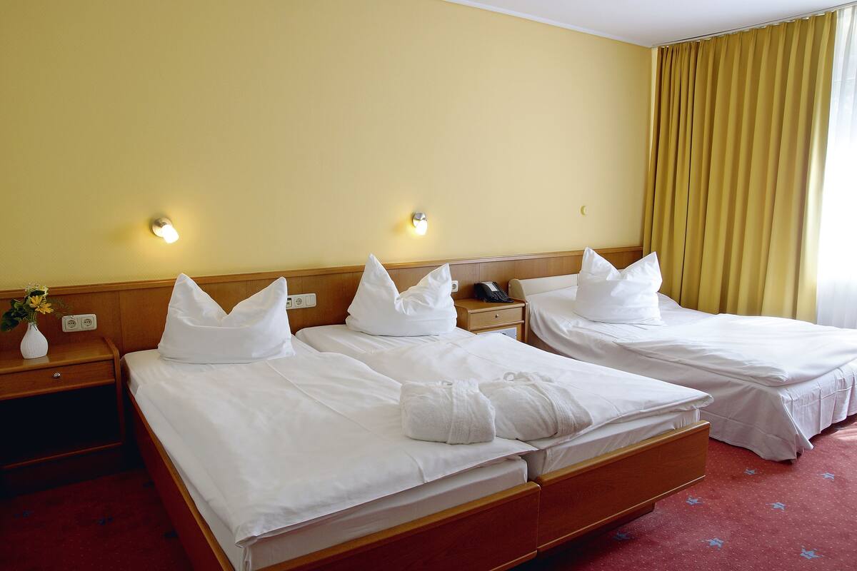 Une chambre d’hôtel avec deux lits, des têtes de lit en bois, des tables de chevet avec des lampes et une moquette rouge.