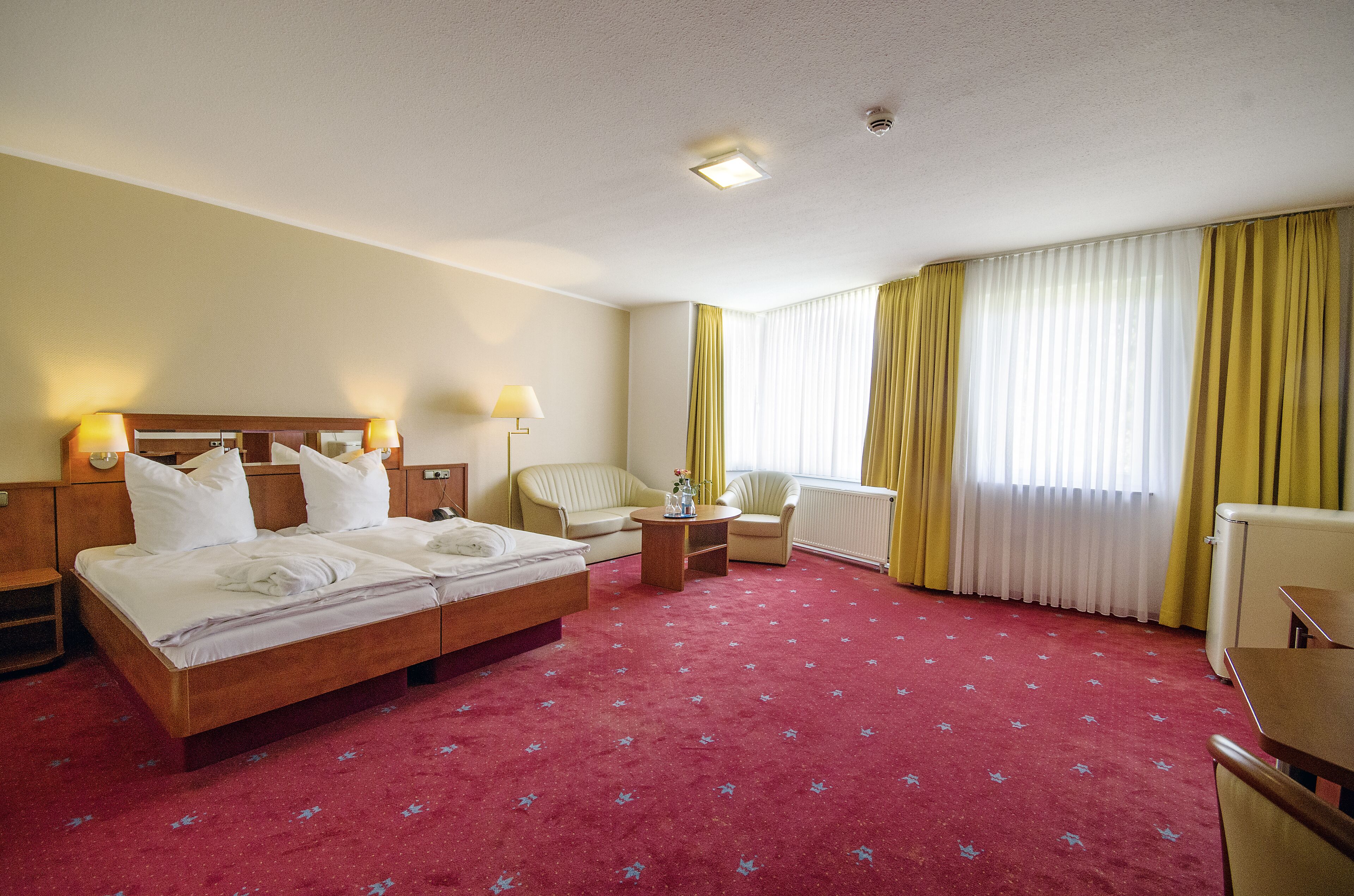 Ein Hotelzimmer mit einem großen Bett, zwei Nachttischen, einem Sessel, einem kleinen Tisch und einer Heizung.