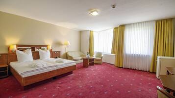 Ein Hotelzimmer mit einem großen Bett, zwei Nachttischen, einem Sessel, einem kleinen Tisch und einer Heizung.