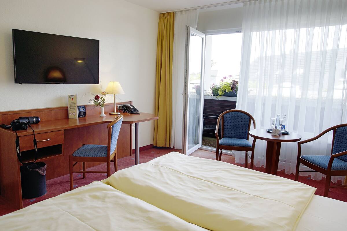 Une chambre d’hôtel équipée d’un lit, d’un bureau avec un ordinateur, d’une chaise, d’une télévision et offrant une vue sur l’extérieur.